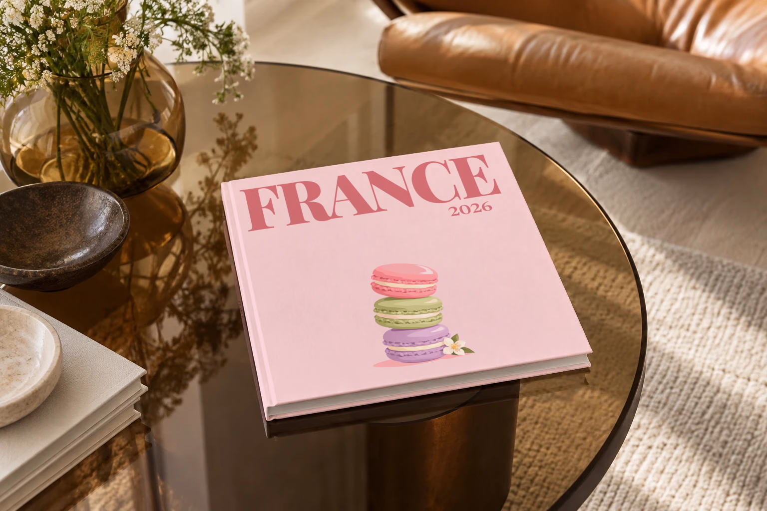 France square hardcover photo book with the illustrated cover of a stack of macarons on pale pink, on a smoked glass coffee table beside a leather armchair in warm afternoon light