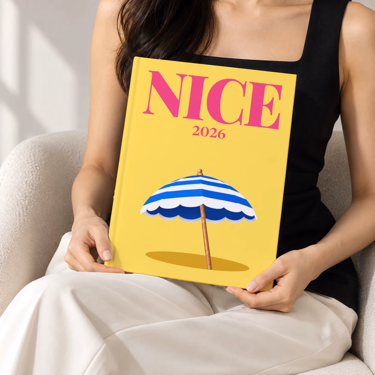 France hardcover photo book with the Nice illustrated cover of a blue and white striped beach umbrella on yellow, held upright in two hands by a woman in a black top, sitting in a cream boucle armchair