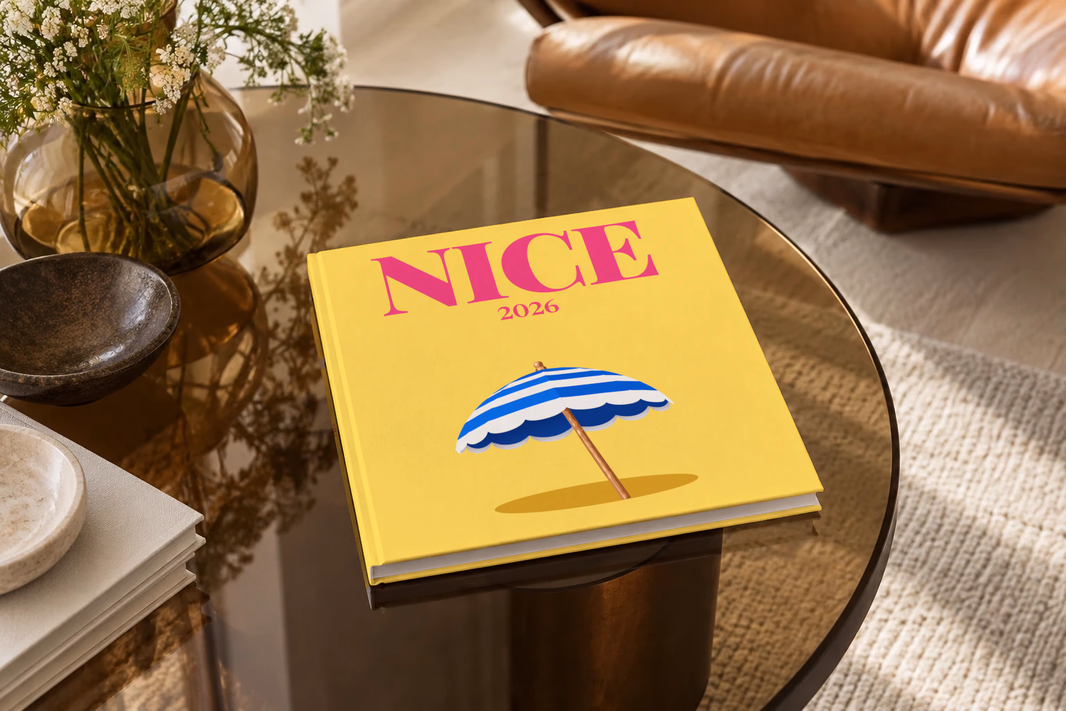 France square hardcover photo book with the Nice illustrated cover of a blue and white striped beach umbrella on yellow, on a smoked glass coffee table beside a leather armchair in warm afternoon light