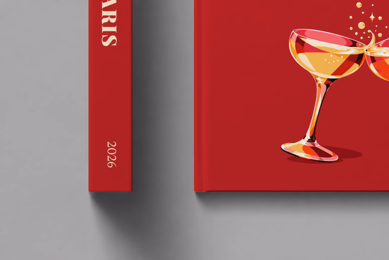 France hardcover photo book with the Paris illustrated cover of two champagne coupes on deep red, shown close up beside its spine on a pale grey studio surface