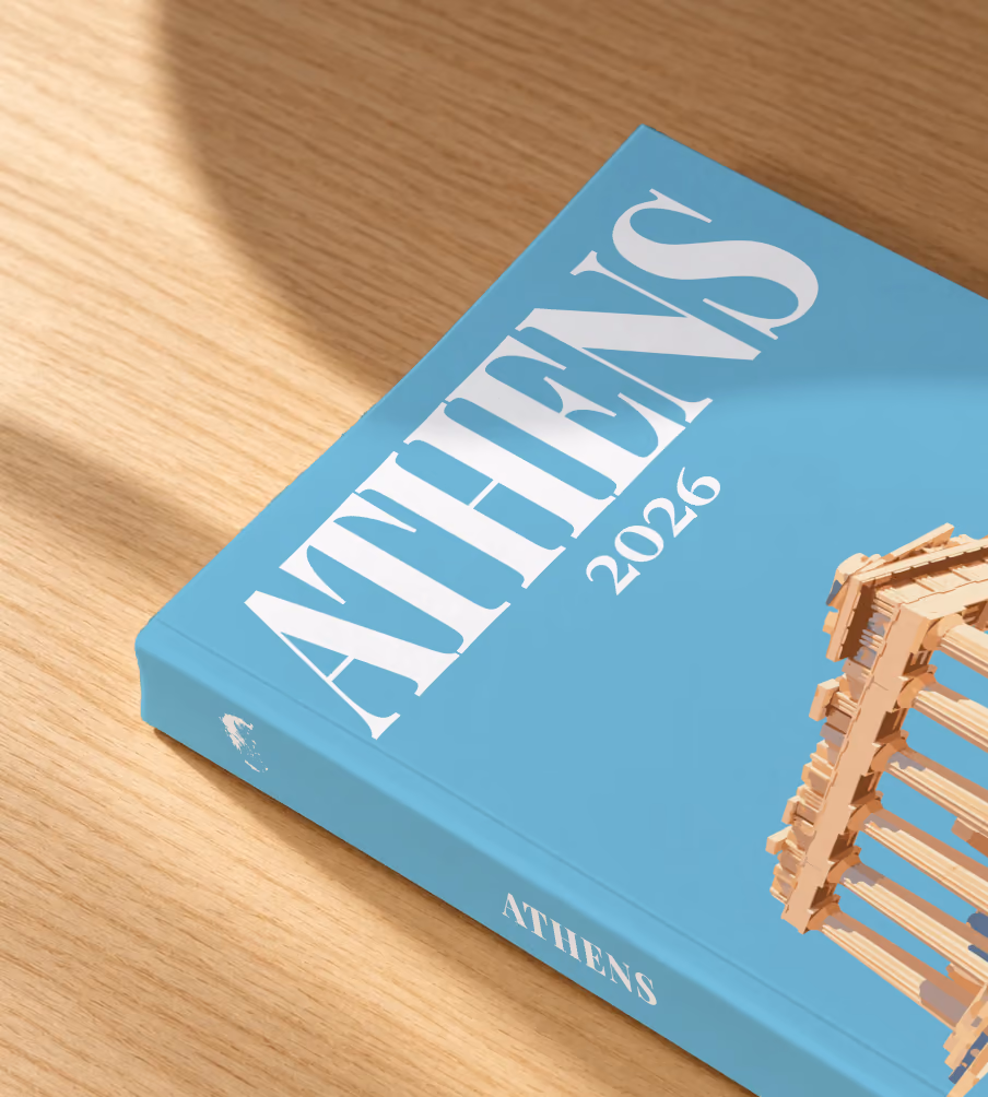 Greece softcover photo book with the Athens illustrated cover of the Parthenon on blue, lying on an oak desk in dappled afternoon sunlight
