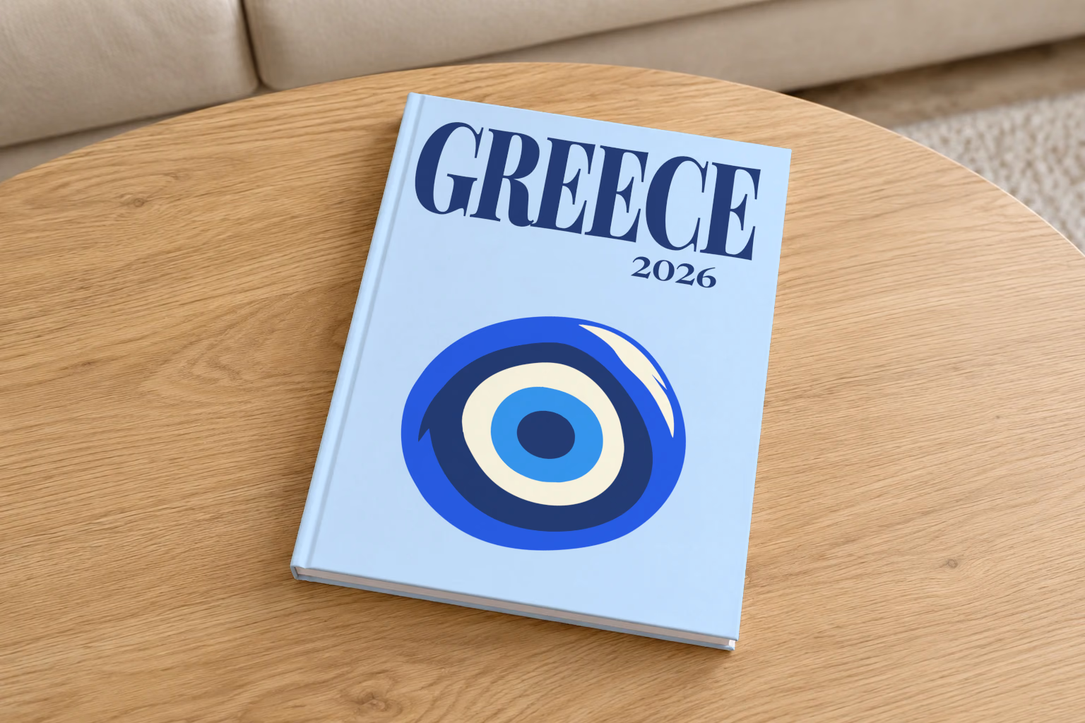 Greece hardcover photo book with the illustrated cover of an evil eye on pale blue, on a round oak coffee table in a bright living room