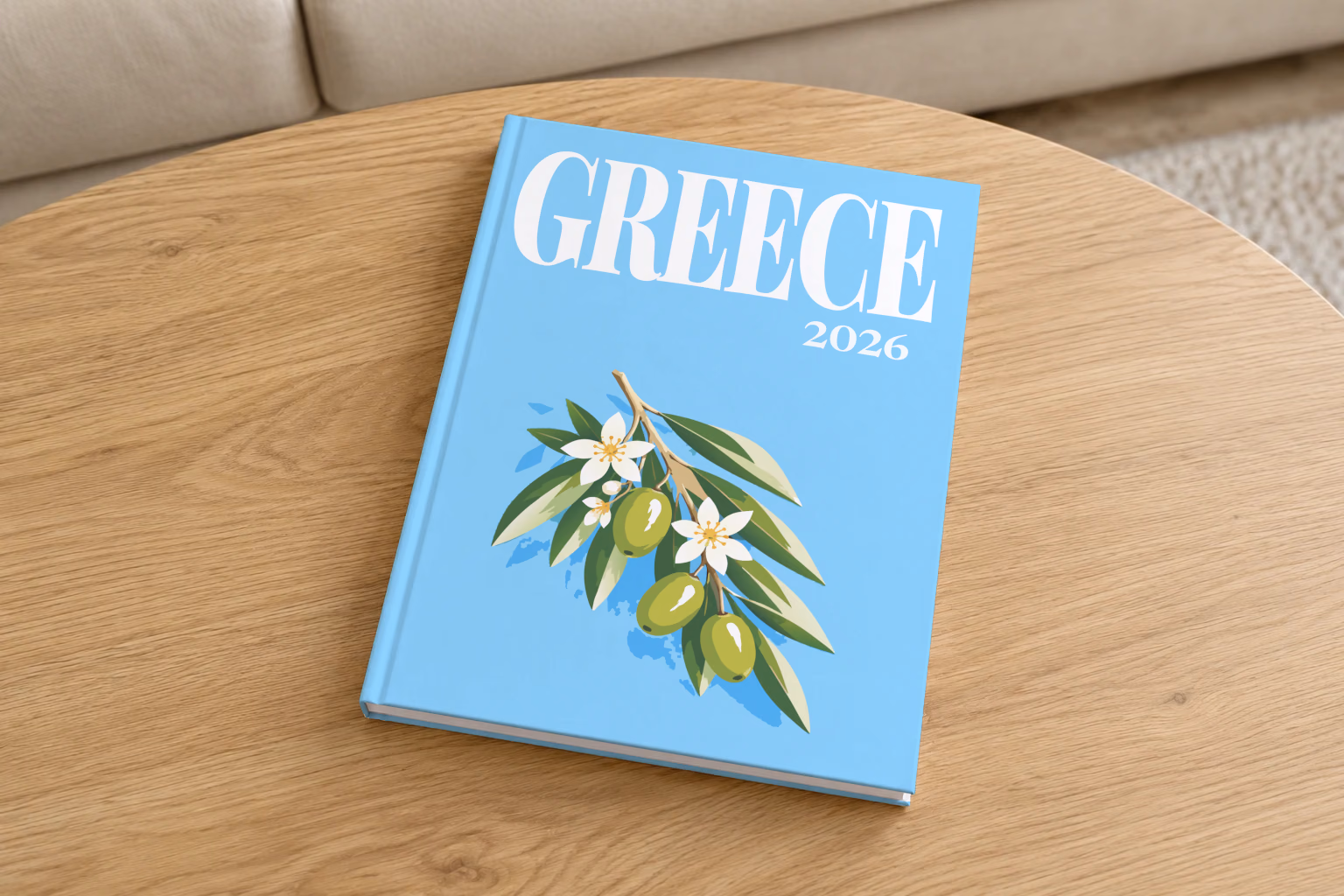 Greece hardcover photo book with the illustrated cover of an olive branch with blossom on sky blue, on a round oak coffee table in a bright living room