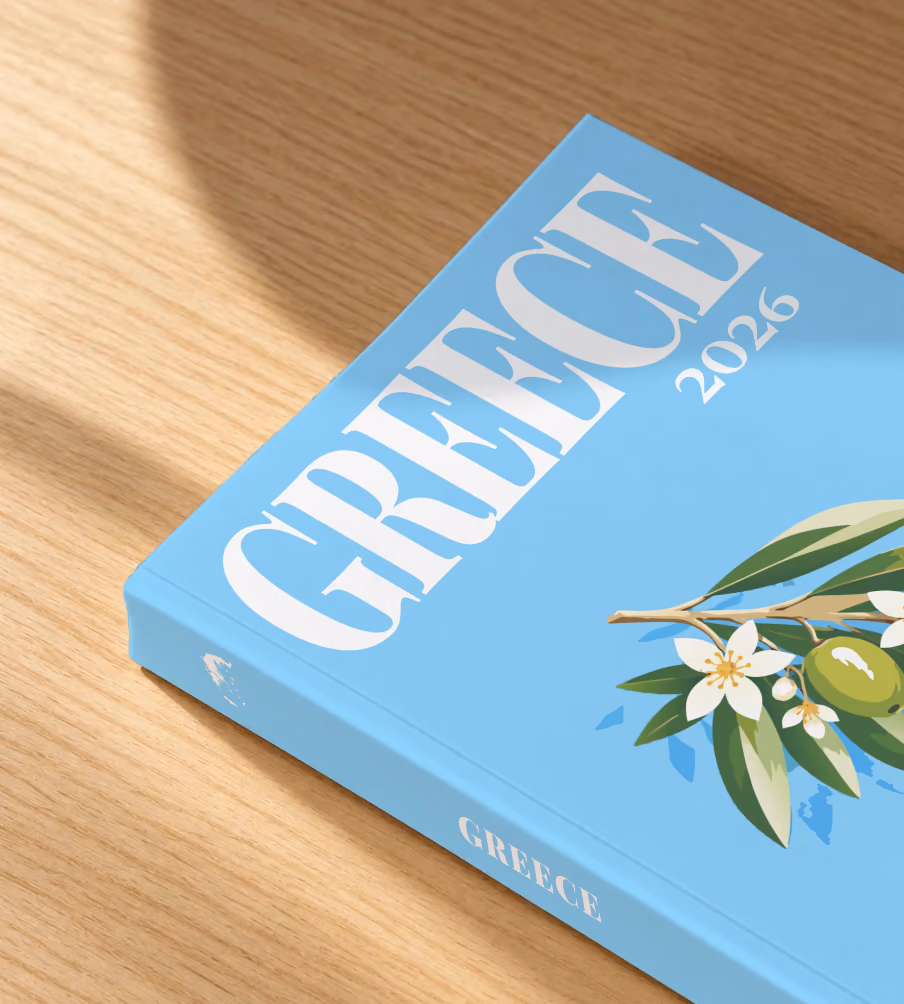 Greece softcover photo book with the illustrated cover of an olive branch with blossom on sky blue, lying on an oak desk in dappled afternoon sunlight