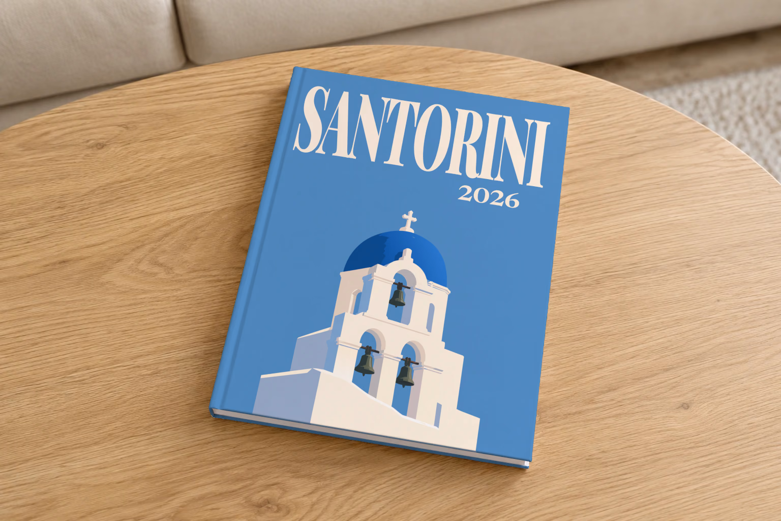 Greece hardcover photo book with the Santorini illustrated cover of a blue-domed bell tower on blue, on a round oak coffee table in a bright living room