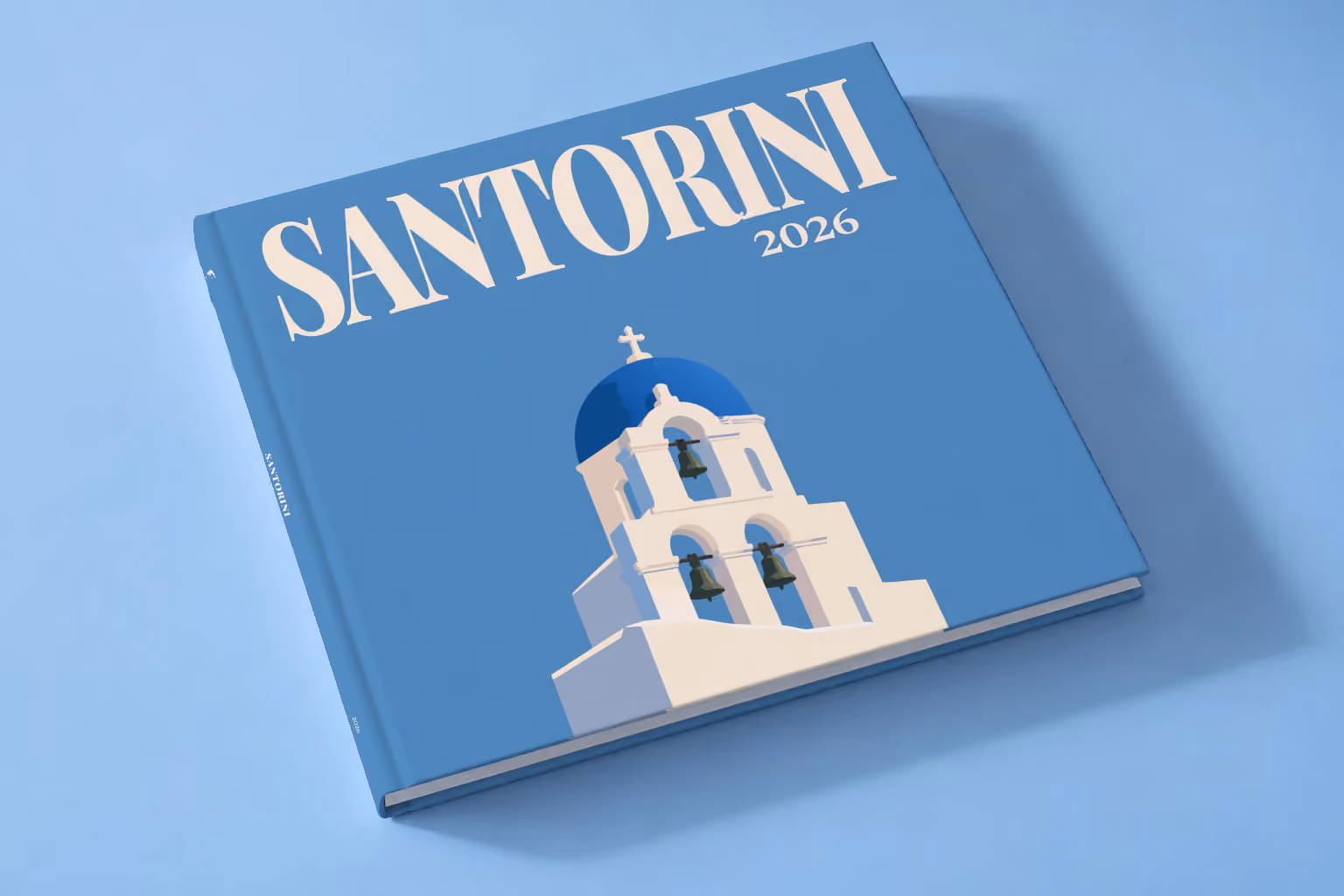 Greece square hardcover photo book with the Santorini illustrated cover of a blue-domed bell tower on blue, lying on a pale blue studio backdrop