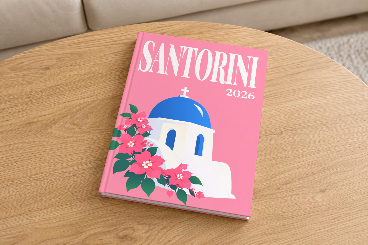 Greece hardcover photo book with the Santorini illustrated cover of a blue-domed chapel and bougainvillea on pink, on a round oak coffee table in a bright living room