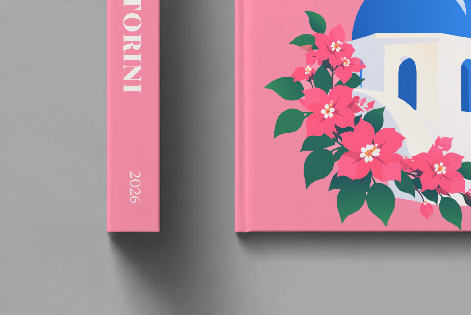 Greece hardcover photo book with the Santorini illustrated cover of a blue-domed chapel and bougainvillea on pink, shown close up beside its spine on a pale grey studio surface