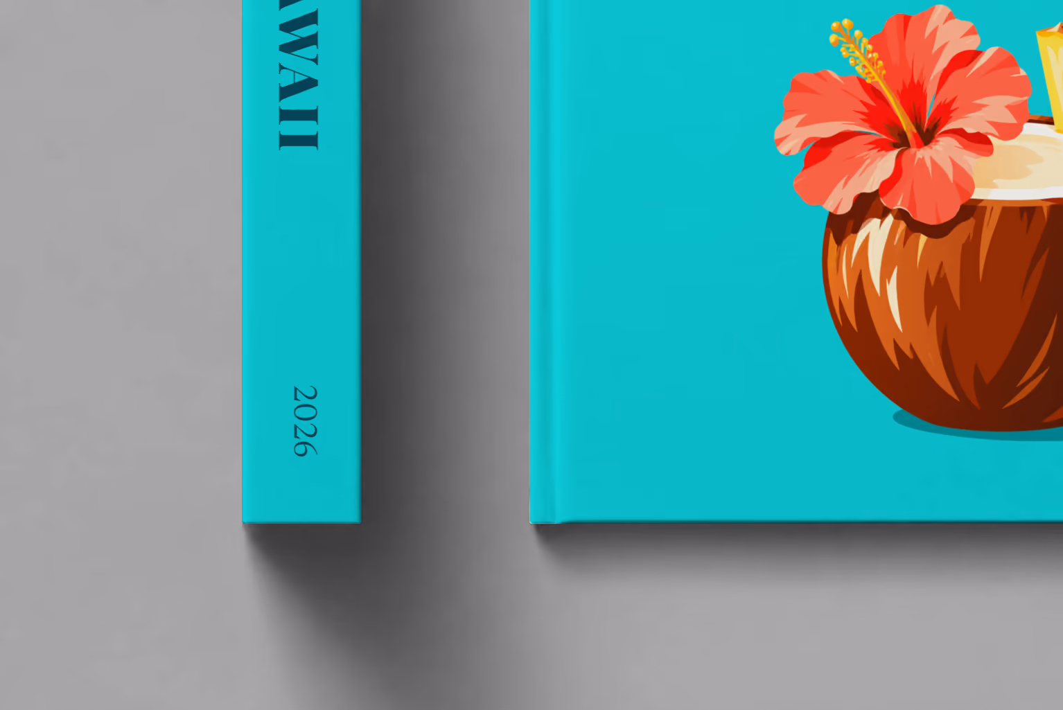 Hawaii hardcover photo book with the illustrated cover of a coconut drink with hibiscus and pineapple on turquoise, shown close up beside its spine on a pale grey studio surface