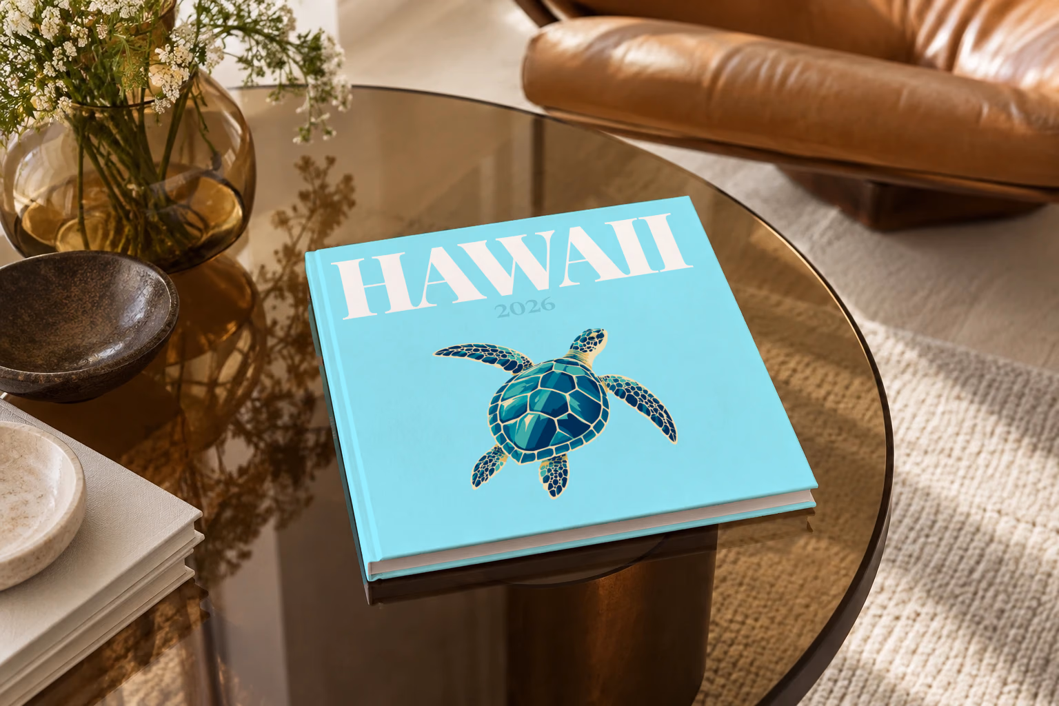 Hawaii square hardcover photo book with the illustrated cover of a green sea turtle on pale aqua, on a smoked glass coffee table beside a leather armchair in warm afternoon light