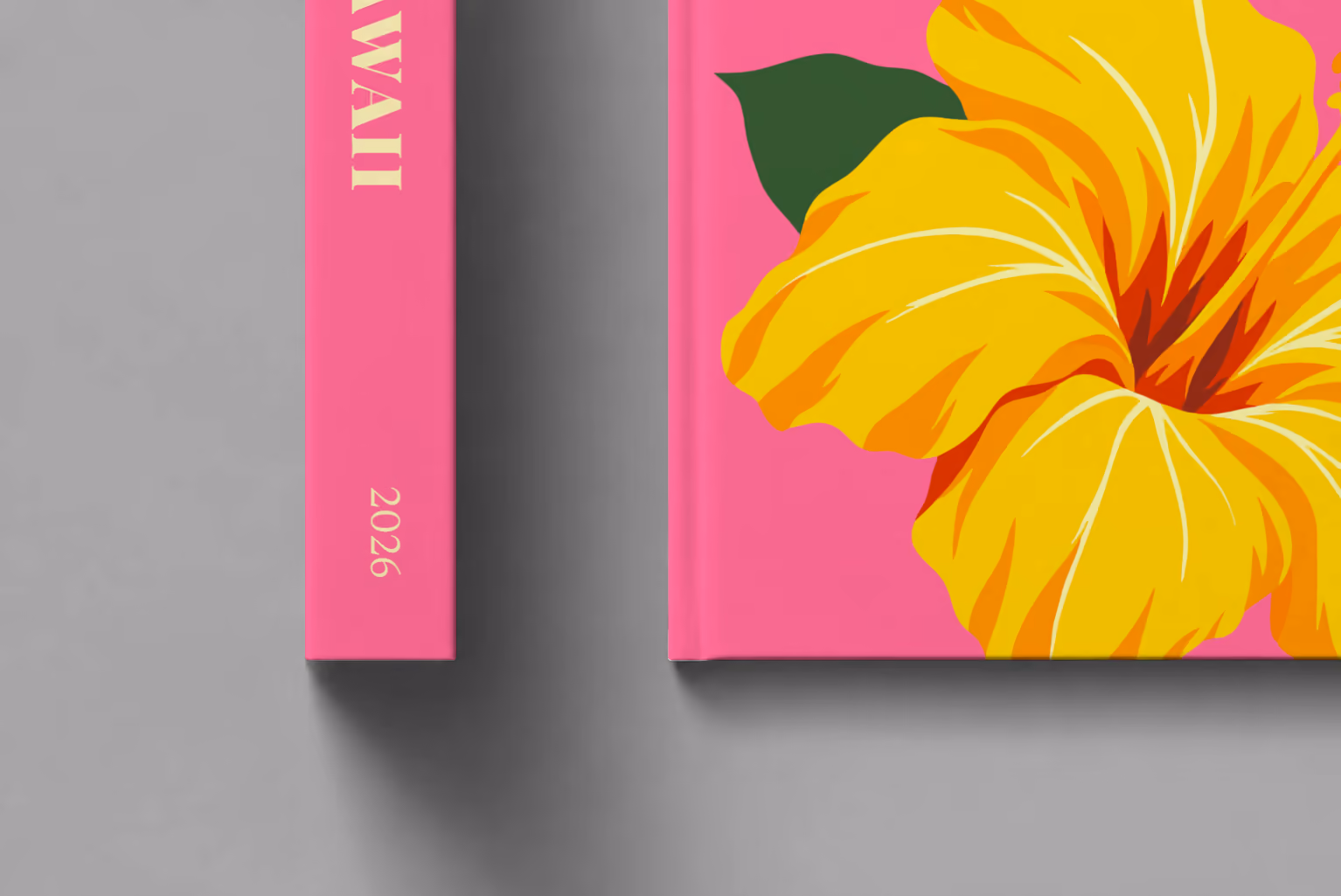 Hawaii hardcover photo book with the illustrated cover of a yellow hibiscus on pink, shown close up beside its spine on a pale grey studio surface