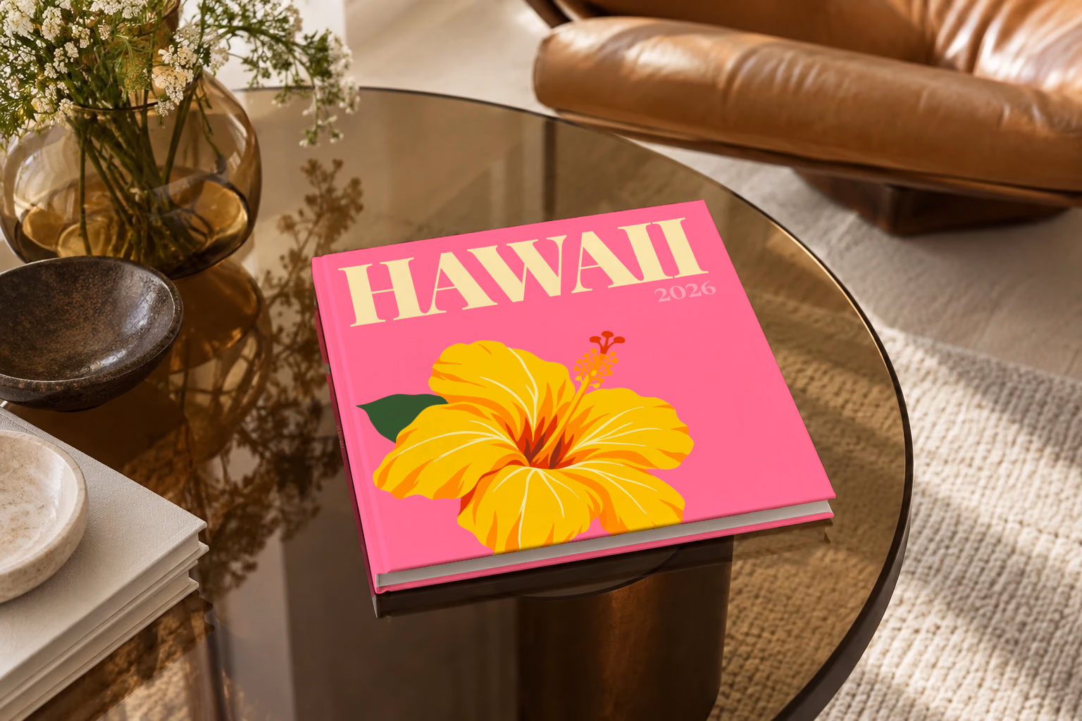 Hawaii square hardcover photo book with the illustrated cover of a yellow hibiscus on pink, on a smoked glass coffee table beside a leather armchair in warm afternoon light
