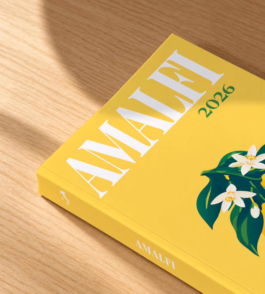 Italy softcover photo book with the Amalfi illustrated cover of lemons and blossom on yellow, lying on an oak desk in dappled afternoon sunlight