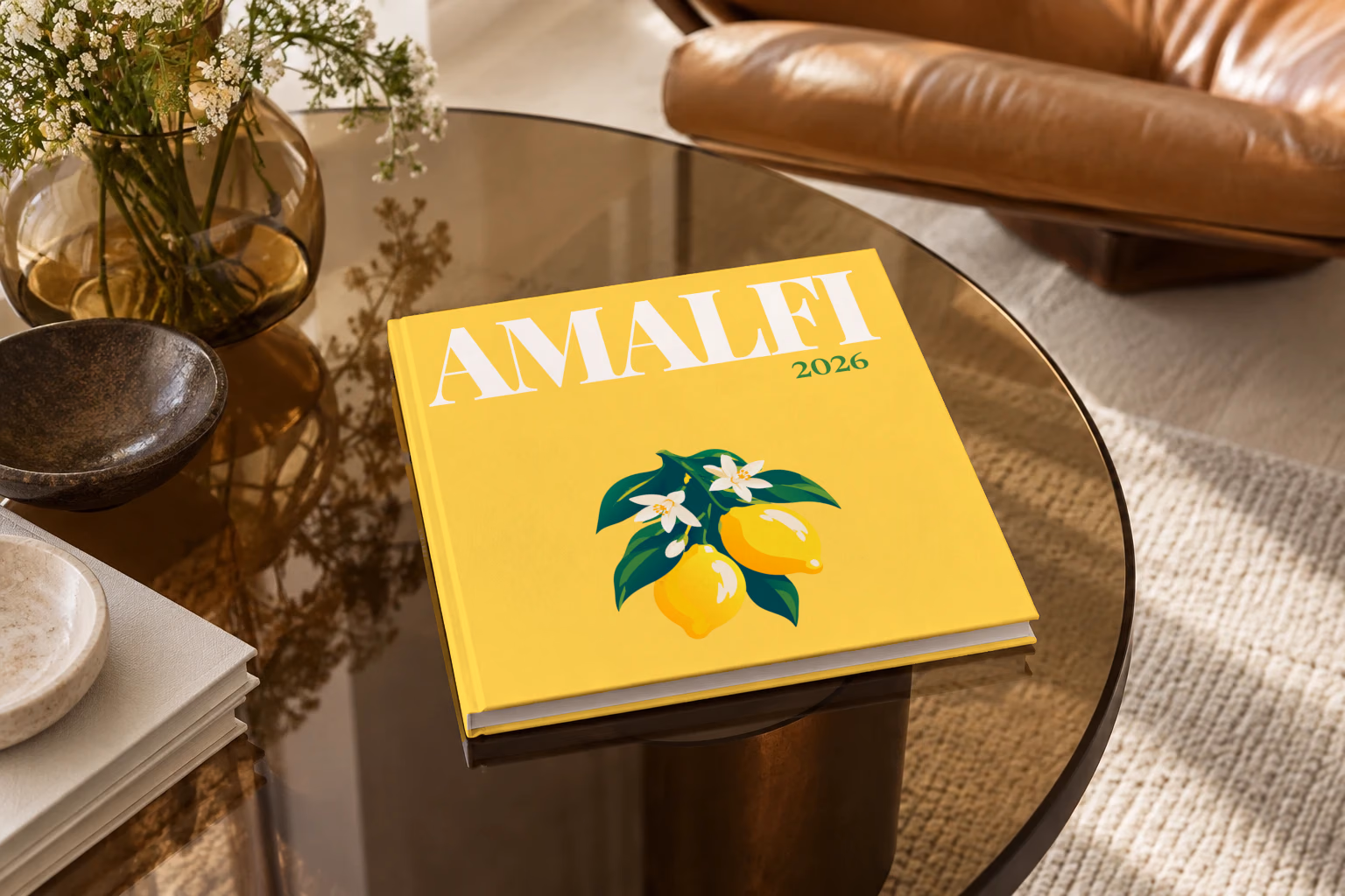 Italy square hardcover photo book with the Amalfi illustrated cover of lemons and blossom on yellow, on a smoked glass coffee table beside a leather armchair in warm afternoon light