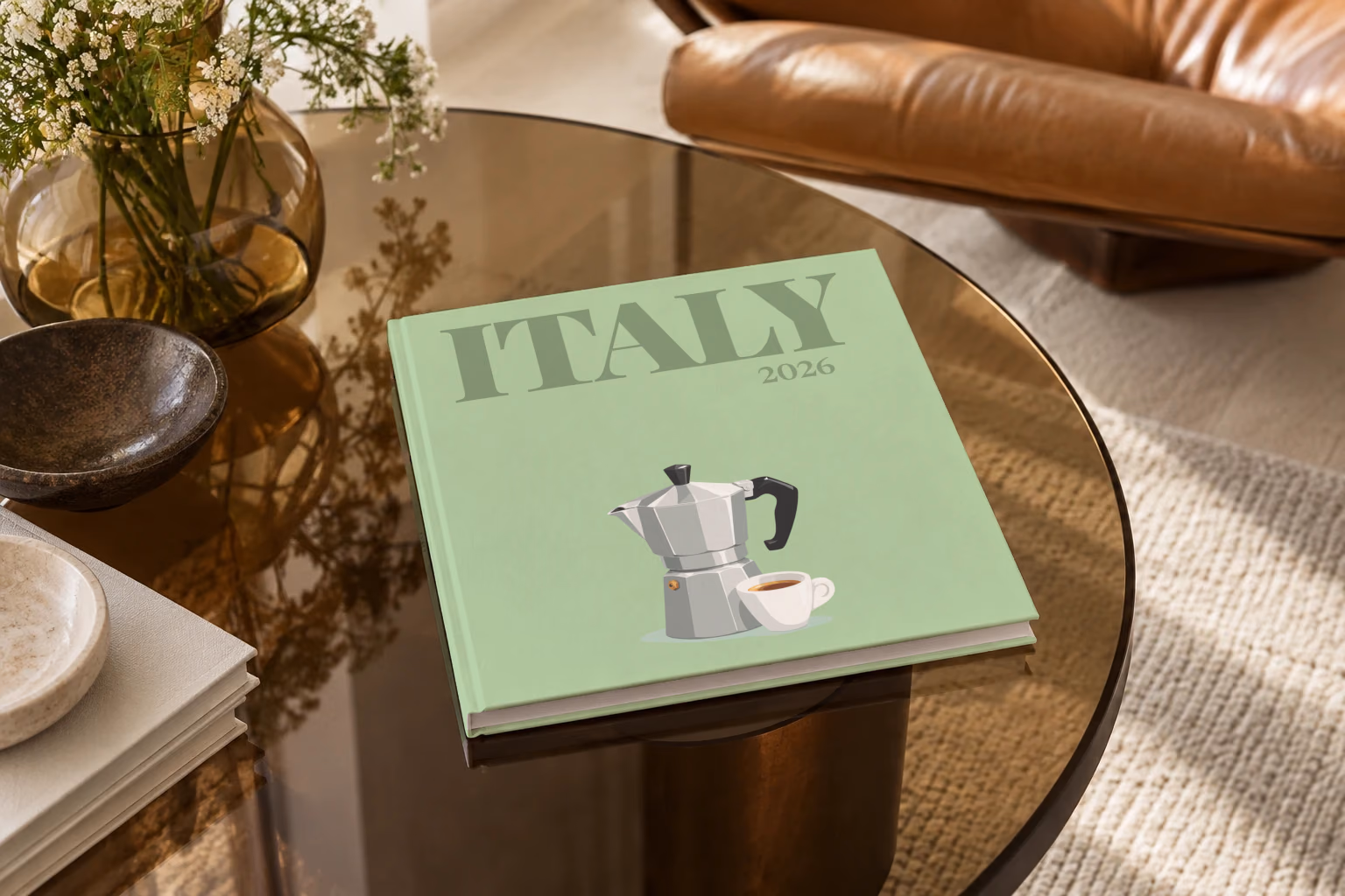 Italy square hardcover photo book with the illustrated cover of a moka pot and an espresso cup on sage green, on a smoked glass coffee table beside a leather armchair in warm afternoon light