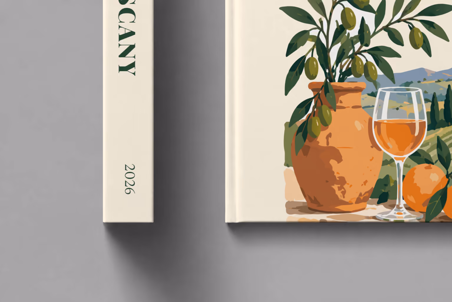 Italy hardcover photo book with the Tuscany illustrated cover of an olive tree, a glass of wine and Tuscan vineyards on cream, shown close up beside its spine on a pale grey studio surface