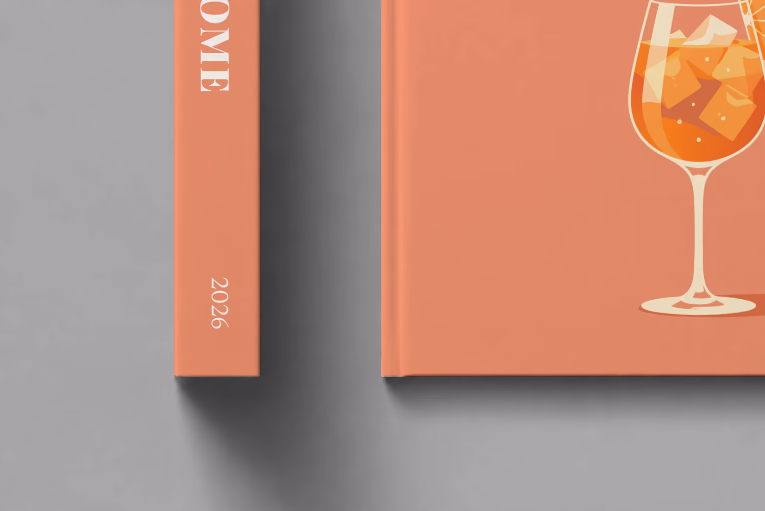 Italy hardcover photo book with the Rome illustrated cover of an Aperol spritz on coral, shown close up beside its spine on a pale grey studio surface