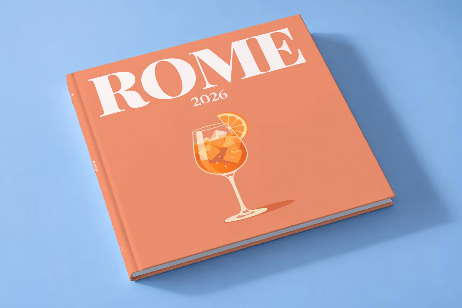 Italy square hardcover photo book with the Rome illustrated cover of an Aperol spritz on coral, lying on a pale blue studio backdrop