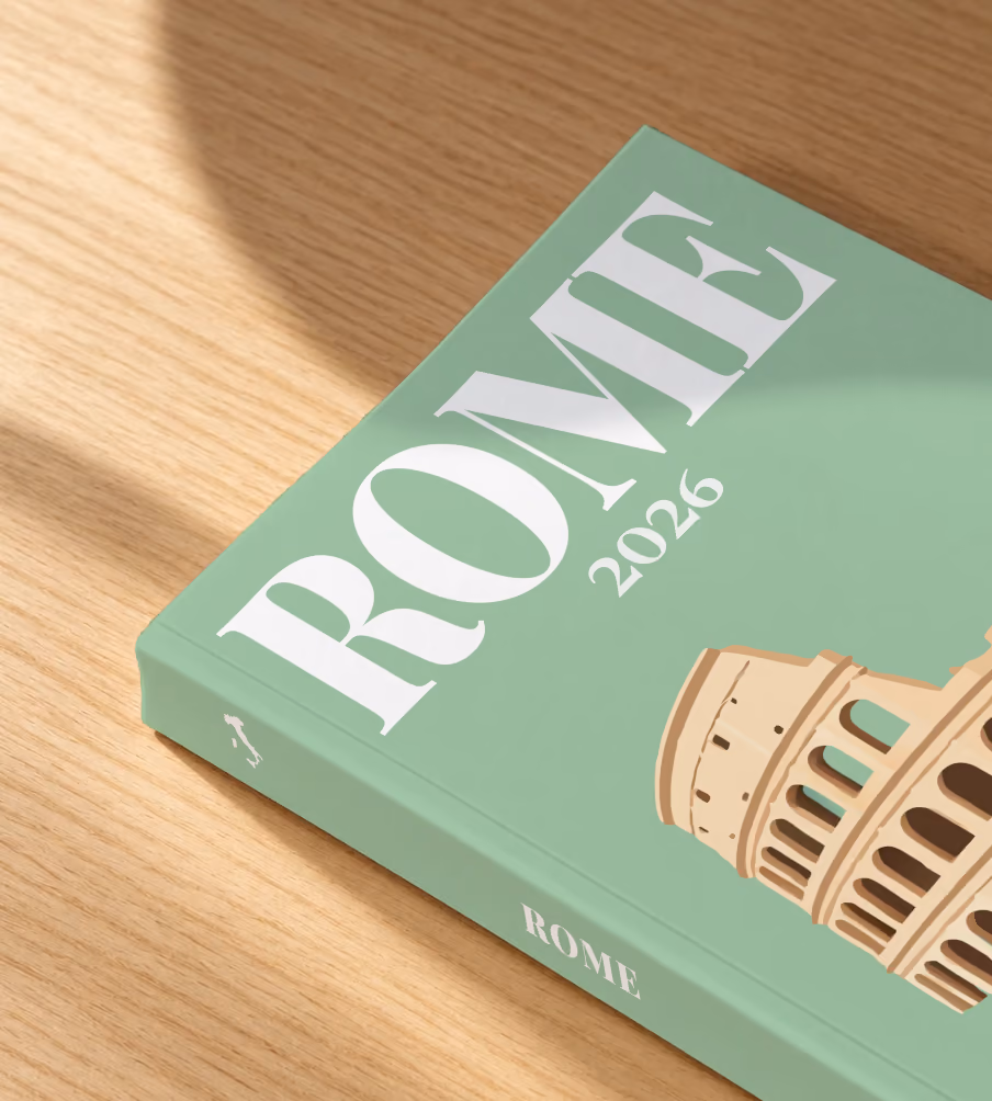 Italy softcover photo book with the Rome illustrated cover of the Colosseum and cypress trees on sage green, lying on an oak desk in dappled afternoon sunlight