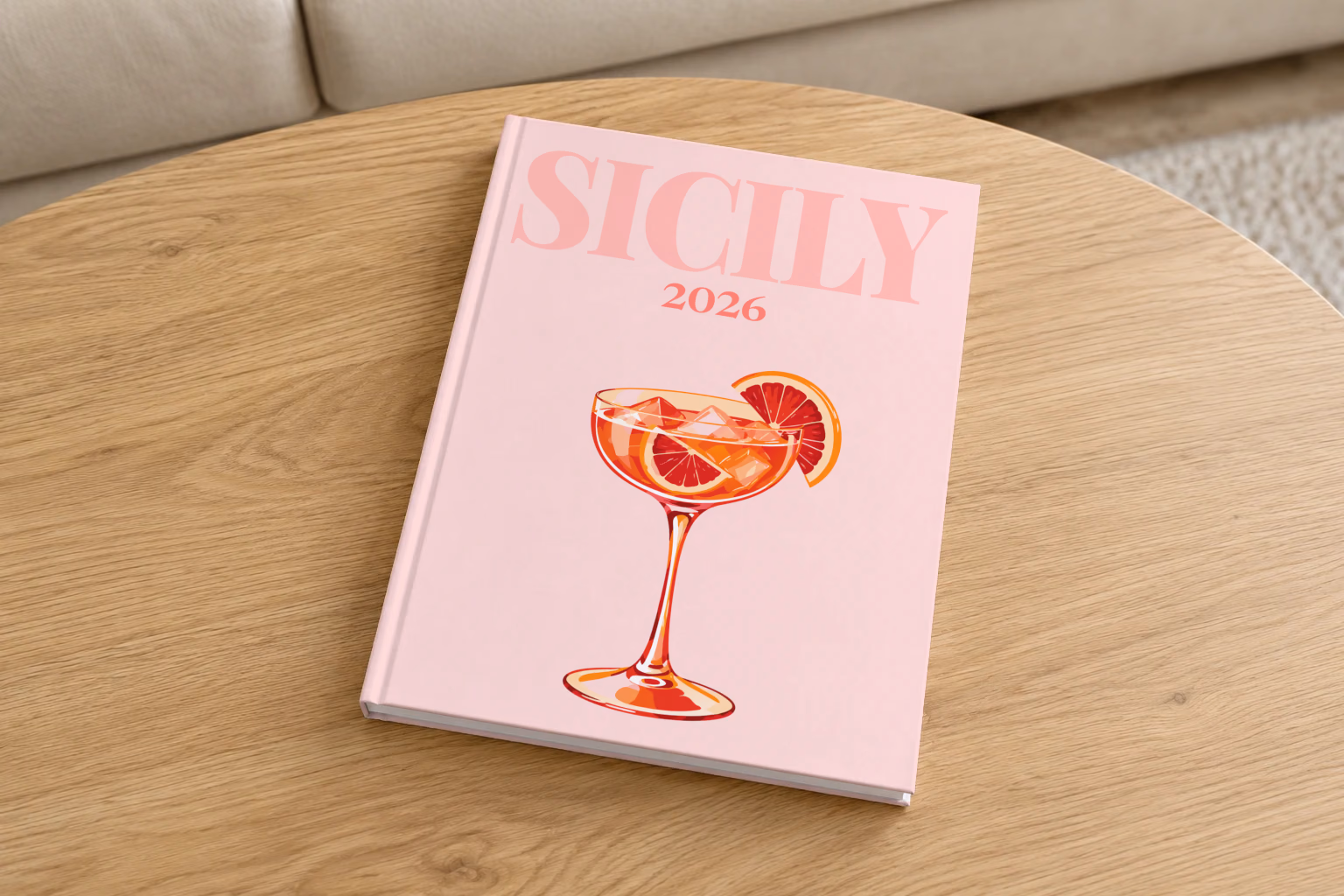 Italy hardcover photo book with the Sicily illustrated cover of a blood orange spritz on pale pink, on a round oak coffee table in a bright living room