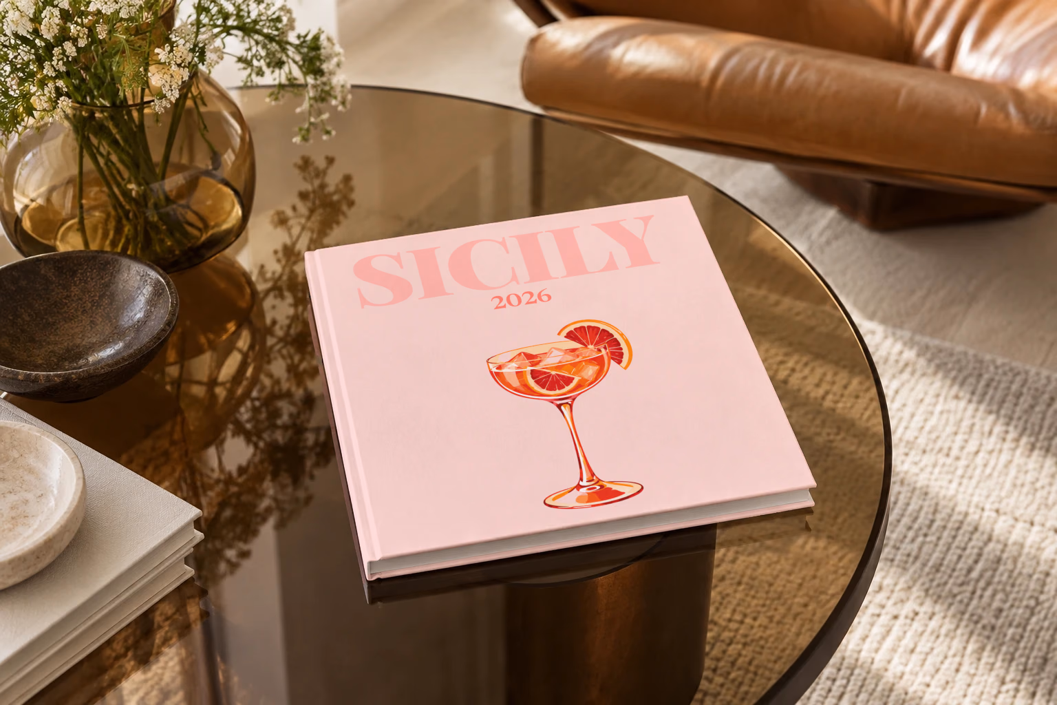 Italy square hardcover photo book with the Sicily illustrated cover of a blood orange spritz on pale pink, on a smoked glass coffee table beside a leather armchair in warm afternoon light