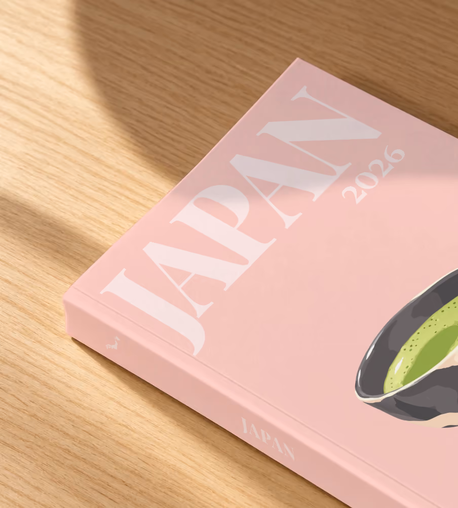 Japan softcover photo book with the illustrated cover of a bowl of matcha and a whisk on pale pink, lying on an oak desk in dappled afternoon sunlight
