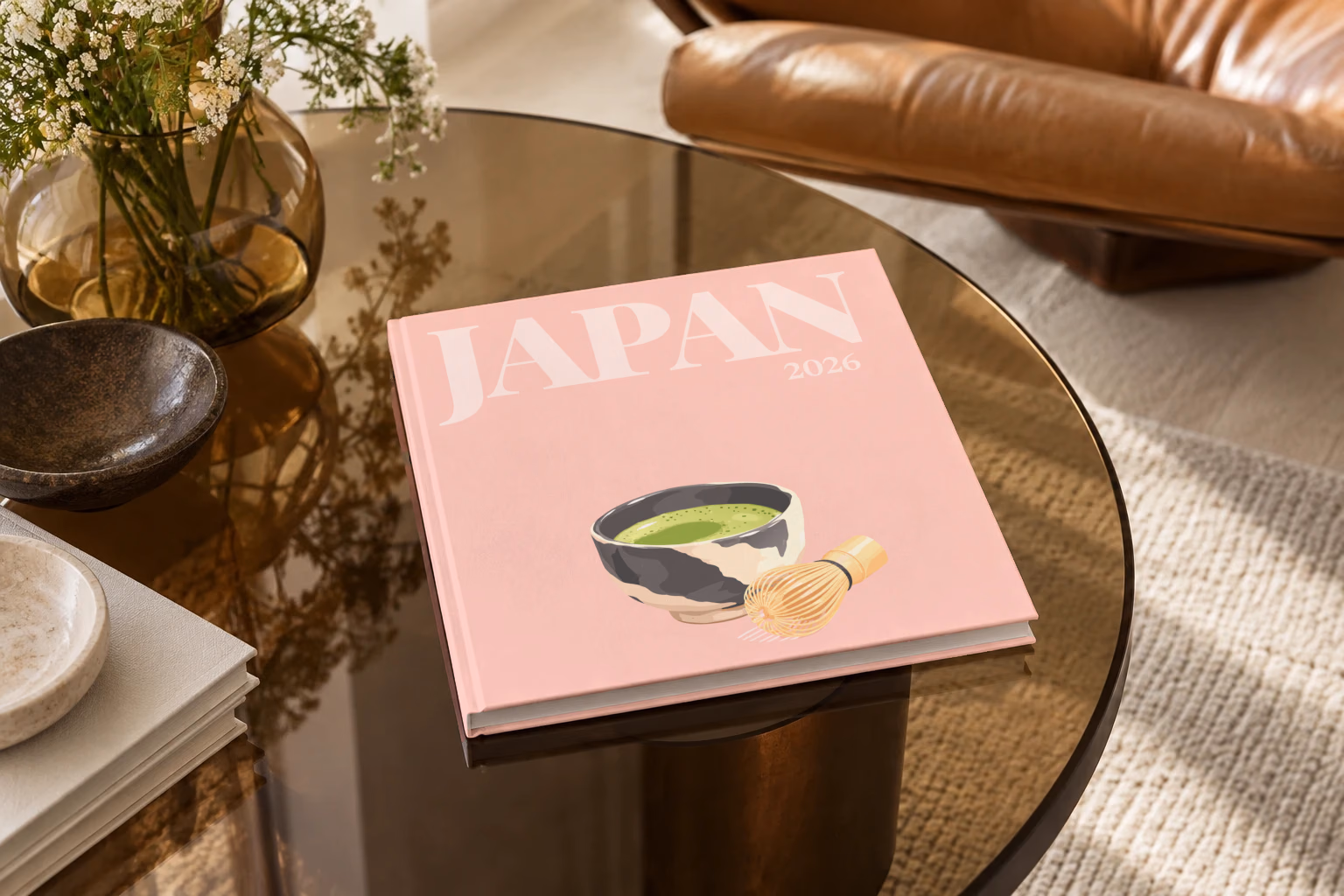 Japan square hardcover photo book with the illustrated cover of a bowl of matcha and a whisk on pale pink, on a smoked glass coffee table beside a leather armchair in warm afternoon light
