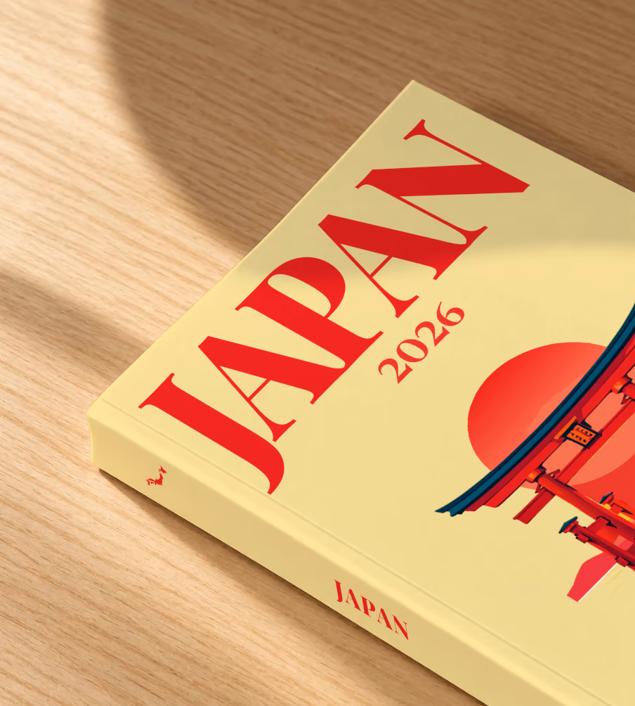 Japan softcover photo book with the illustrated cover of a torii gate in the water at sunset on pale yellow, lying on an oak desk in dappled afternoon sunlight