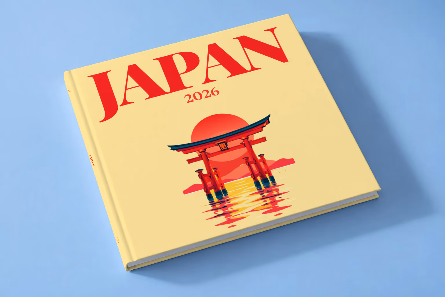 Japan square hardcover photo book with the illustrated cover of a torii gate in the water at sunset on pale yellow, lying on a pale blue studio backdrop