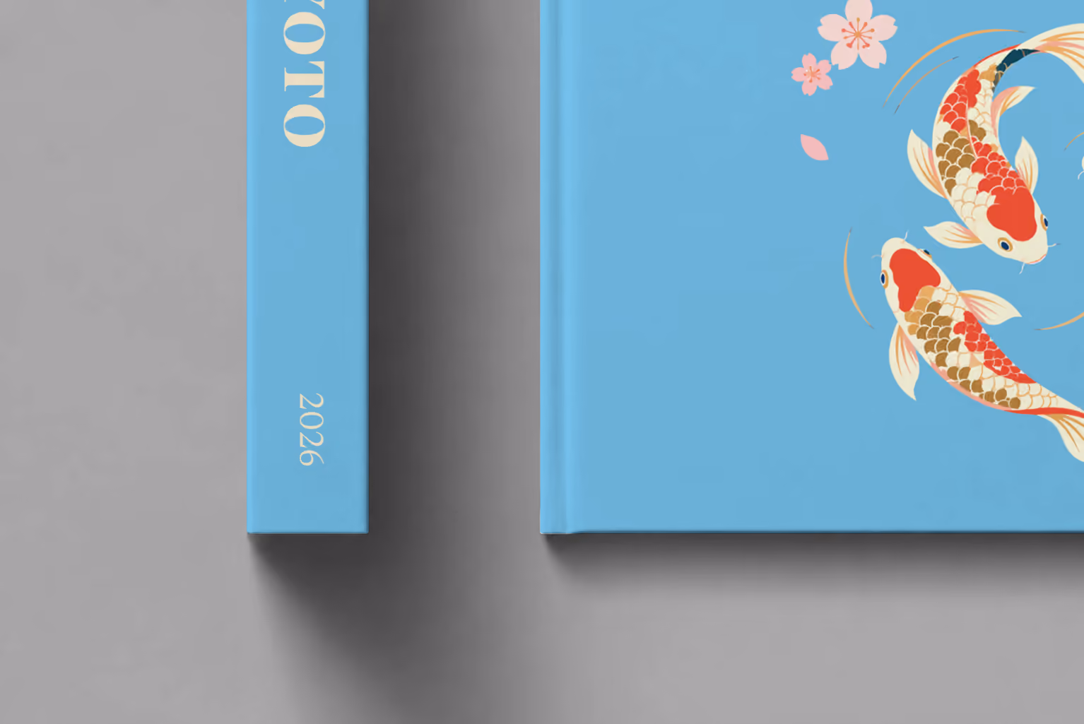 Japan hardcover photo book with the Kyoto illustrated cover of koi and cherry blossom on sky blue, shown close up beside its spine on a pale grey studio surface