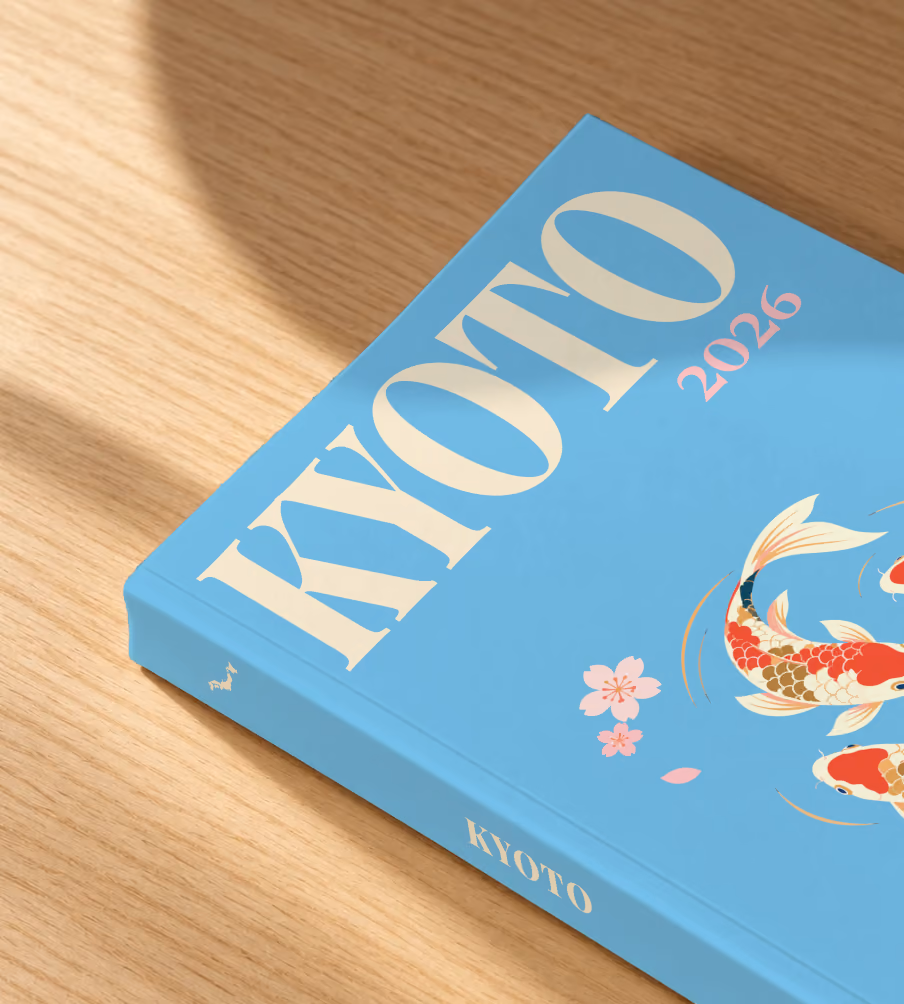 Japan softcover photo book with the Kyoto illustrated cover of koi and cherry blossom on sky blue, lying on an oak desk in dappled afternoon sunlight