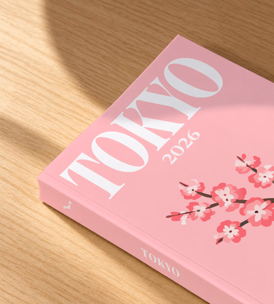 Japan softcover photo book with the Tokyo illustrated cover of a cherry blossom branch on pink, lying on an oak desk in dappled afternoon sunlight