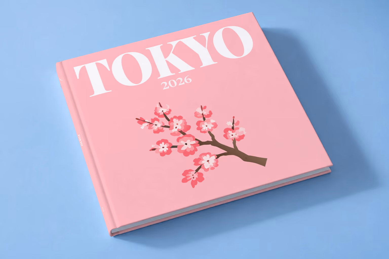 Japan square hardcover photo book with the Tokyo illustrated cover of a cherry blossom branch on pink, lying on a pale blue studio backdrop