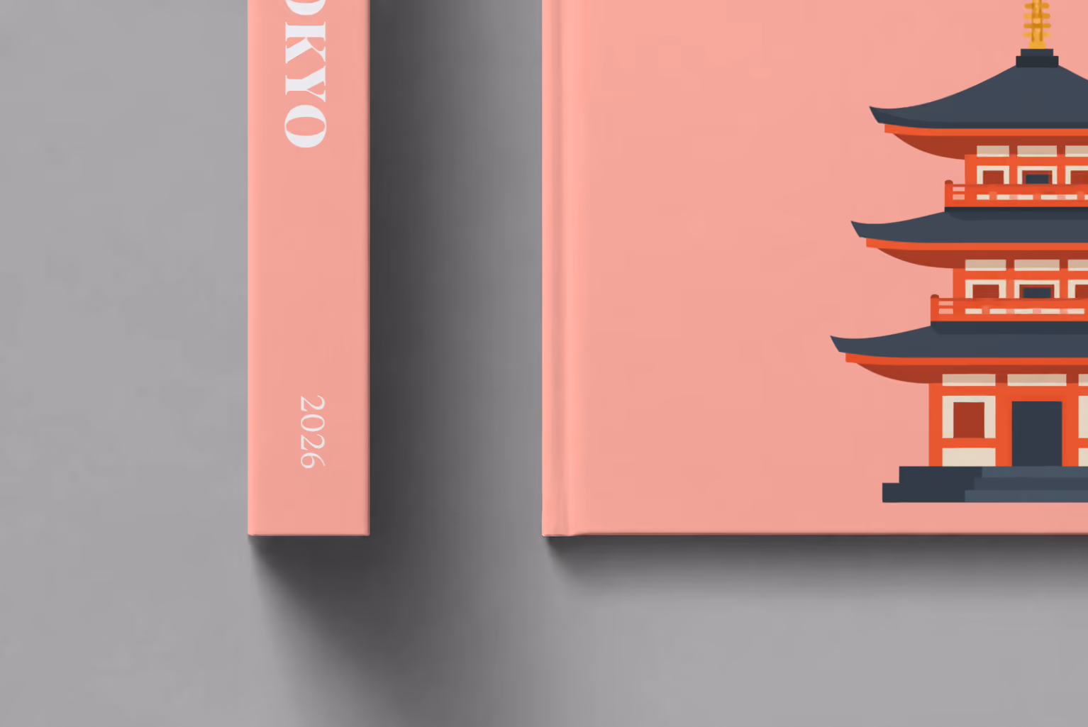 Japan hardcover photo book with the Tokyo illustrated cover of a pagoda on salmon pink, shown close up beside its spine on a pale grey studio surface