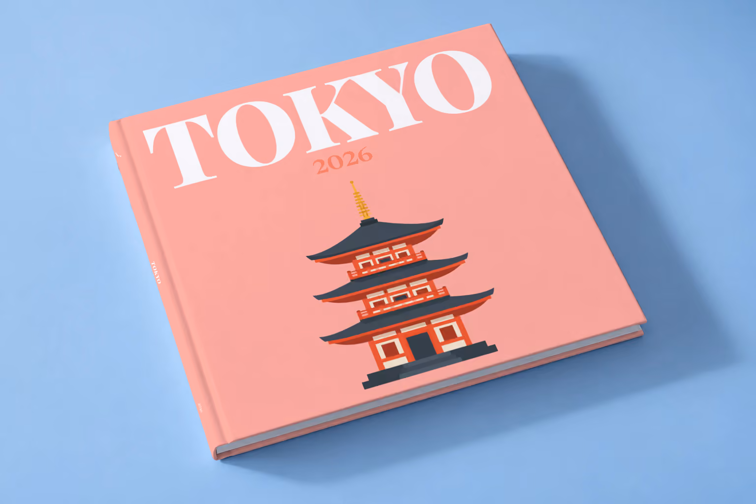 Japan square hardcover photo book with the Tokyo illustrated cover of a pagoda on salmon pink, lying on a pale blue studio backdrop