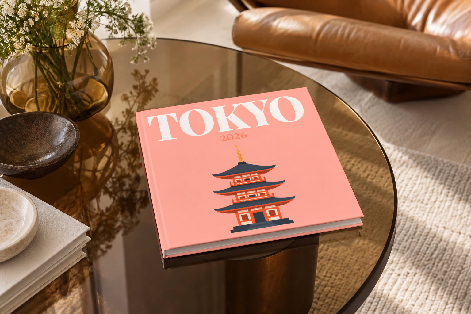 Japan square hardcover photo book with the Tokyo illustrated cover of a pagoda on salmon pink, on a smoked glass coffee table beside a leather armchair in warm afternoon light
