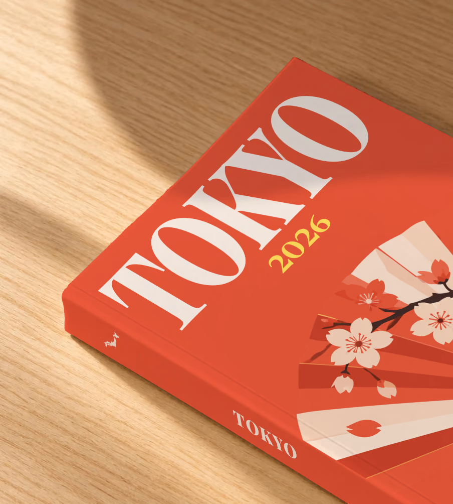 Japan softcover photo book with the Tokyo illustrated cover of a folding fan with cherry blossom on red, lying on an oak desk in dappled afternoon sunlight