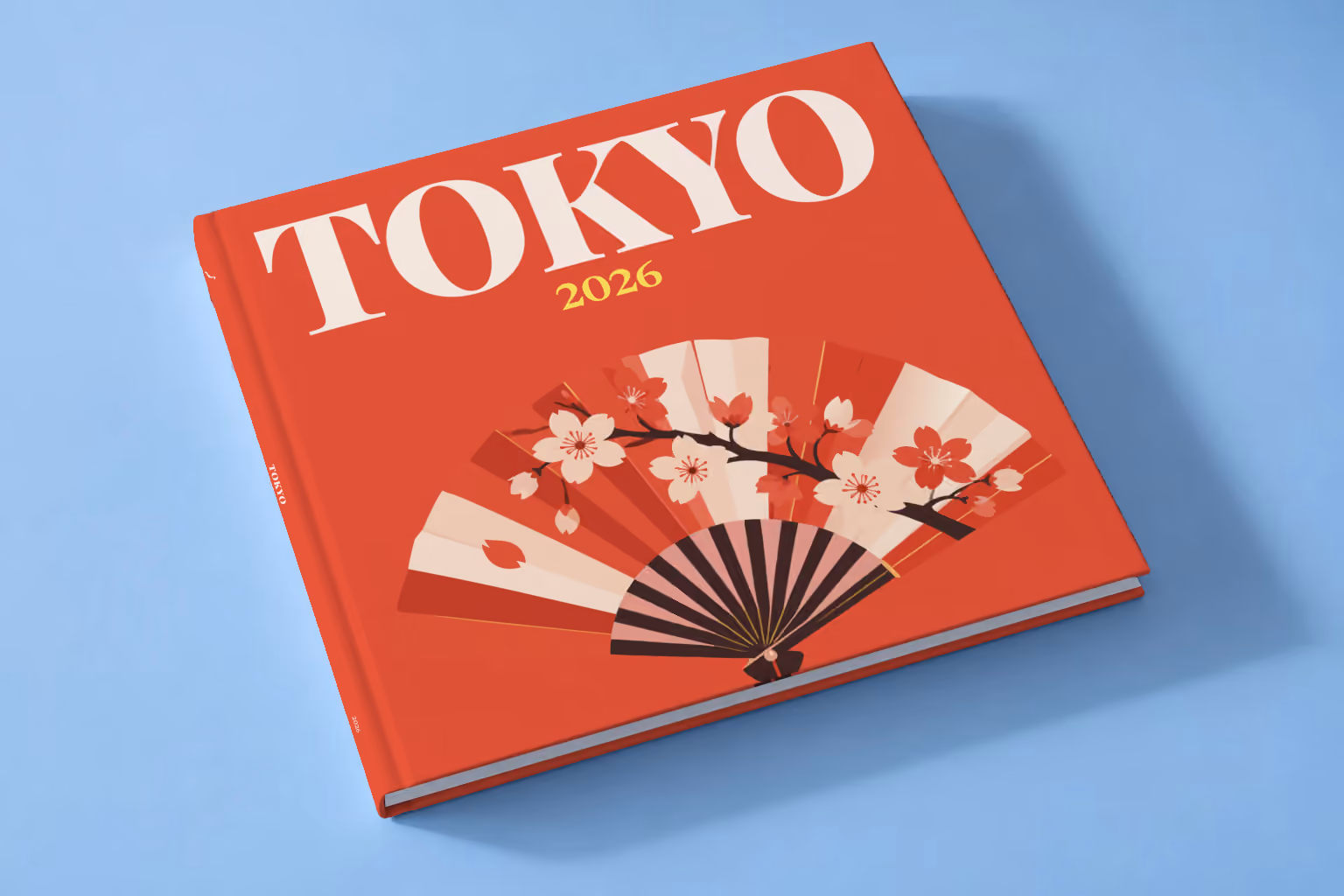 Japan square hardcover photo book with the Tokyo illustrated cover of a folding fan with cherry blossom on red, lying on a pale blue studio backdrop