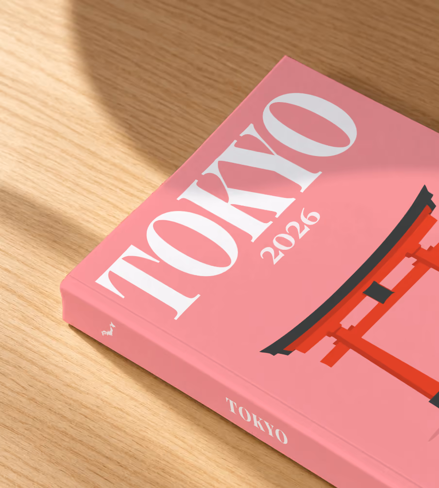 Japan softcover photo book with the Tokyo illustrated cover of a red torii gate and petals on pink, lying on an oak desk in dappled afternoon sunlight