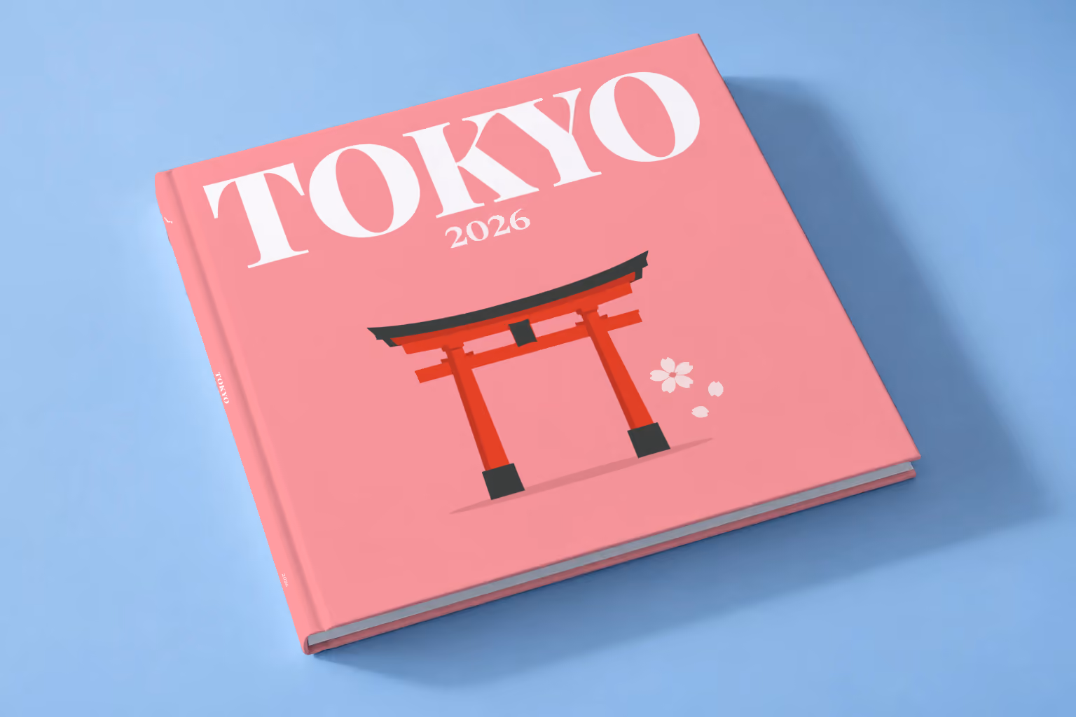 Japan square hardcover photo book with the Tokyo illustrated cover of a red torii gate and petals on pink, lying on a pale blue studio backdrop