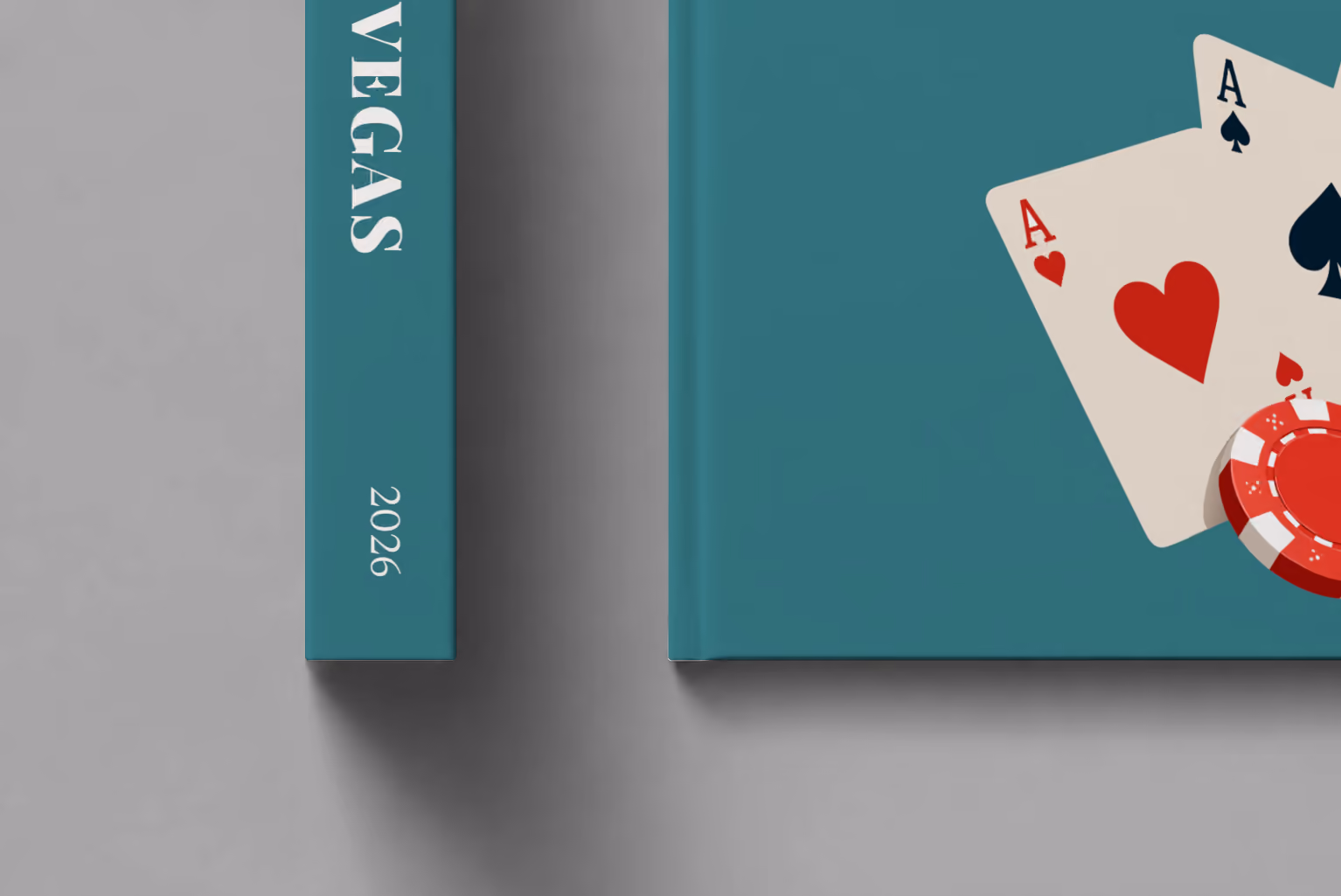 Las Vegas hardcover photo book with the illustrated cover of playing card aces and a red casino chip on teal, shown close up beside its spine on a pale grey studio surface