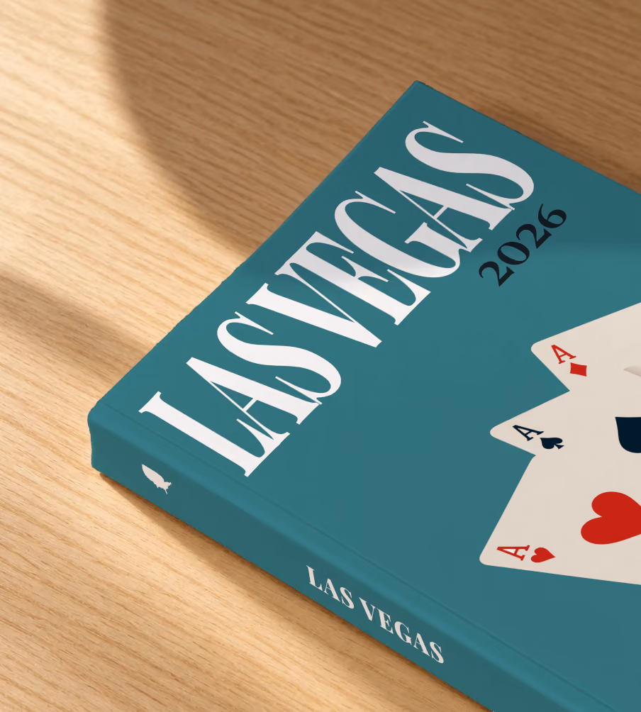 Las Vegas softcover photo book with the illustrated cover of playing card aces and a red casino chip on teal, lying on an oak desk in dappled afternoon sunlight