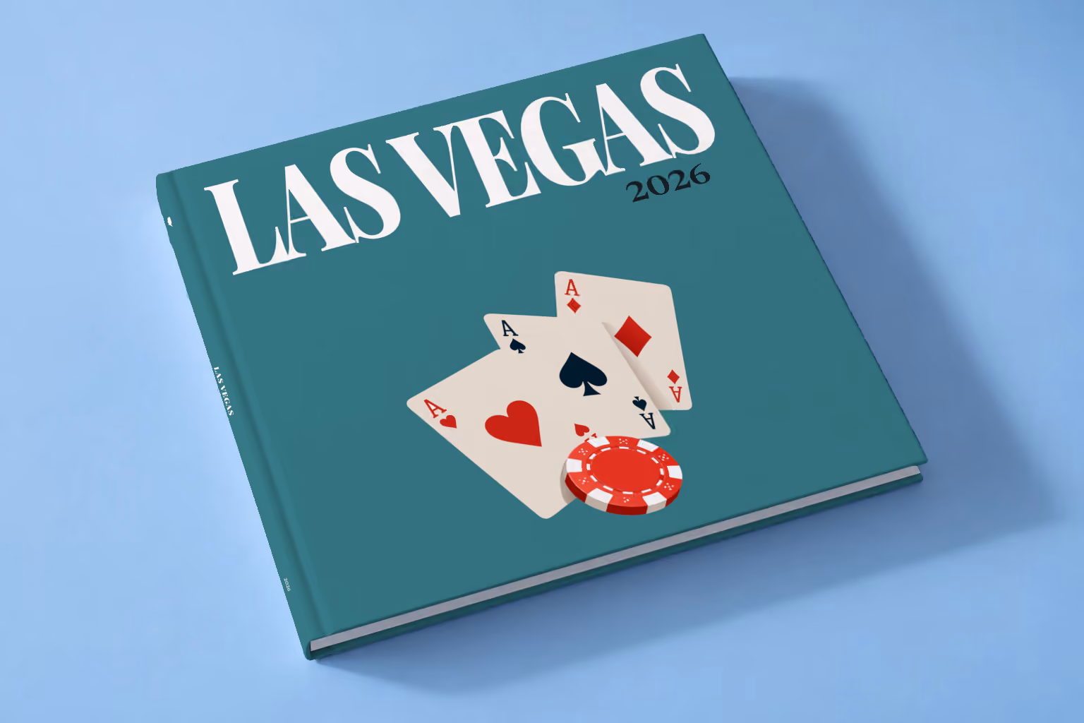 Las Vegas square hardcover photo book with the illustrated cover of playing card aces and a red casino chip on teal, lying on a pale blue studio backdrop