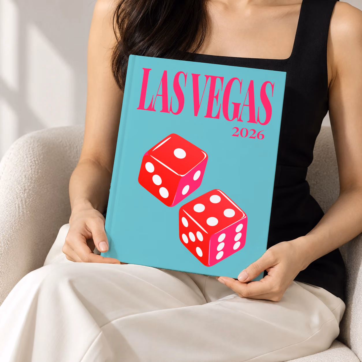 Las Vegas hardcover photo book with the illustrated cover of a pair of red casino dice on turquoise, held upright in two hands by a woman in a black top, sitting in a cream boucle armchair