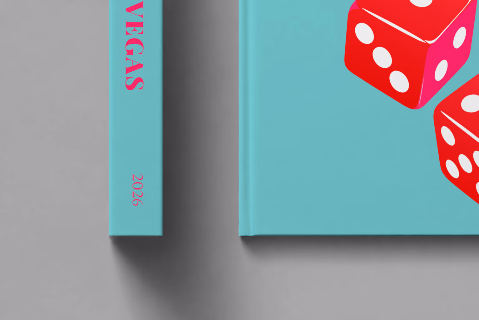 Las Vegas hardcover photo book with the illustrated cover of a pair of red casino dice on turquoise, shown close up beside its spine on a pale grey studio surface