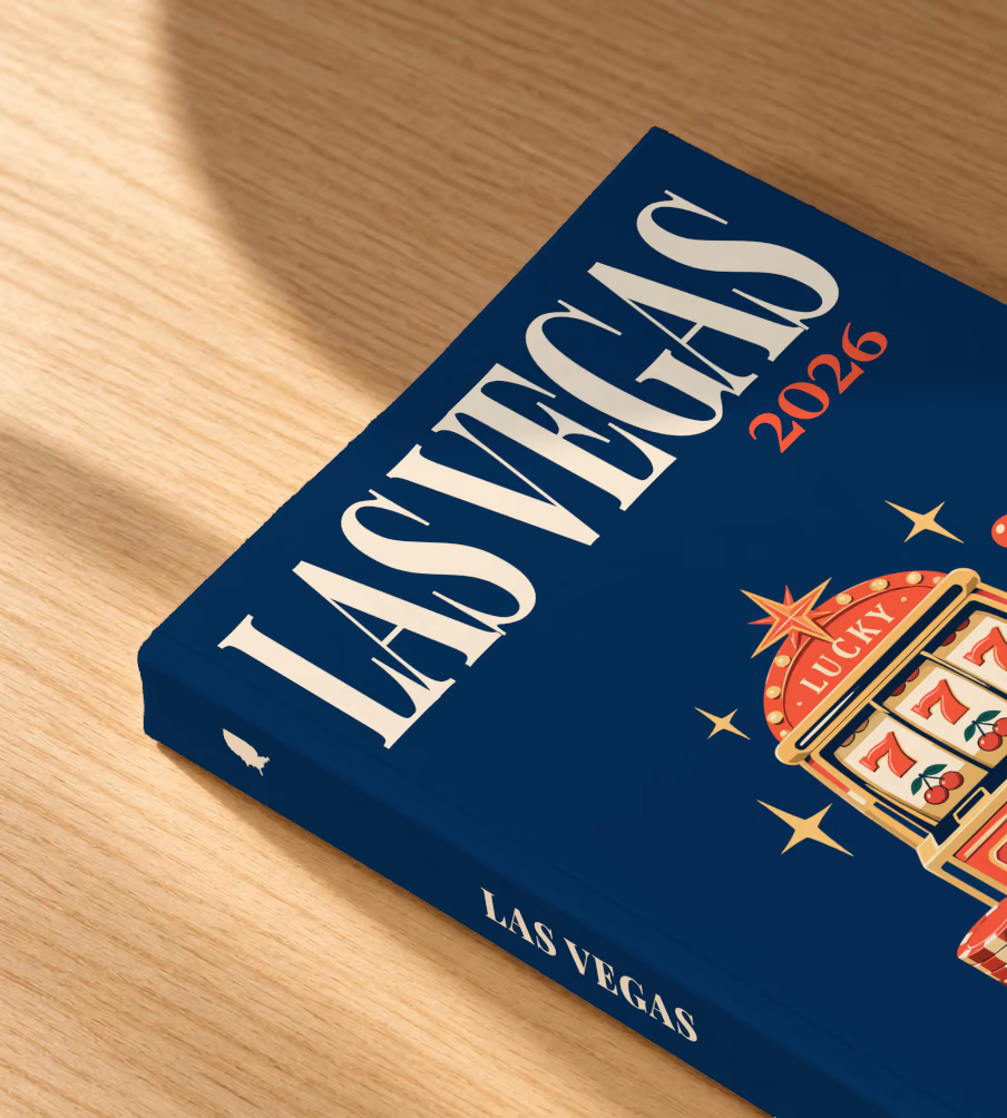 Las Vegas softcover photo book with the illustrated cover of a lucky 777 jackpot slot machine with casino chips and cards on navy, lying on an oak desk in dappled afternoon sunlight