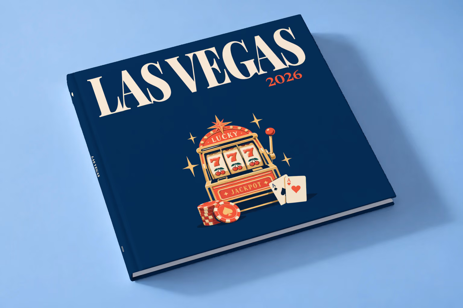 Las Vegas square hardcover photo book with the illustrated cover of a lucky 777 jackpot slot machine with casino chips and cards on navy, lying on a pale blue studio backdrop
