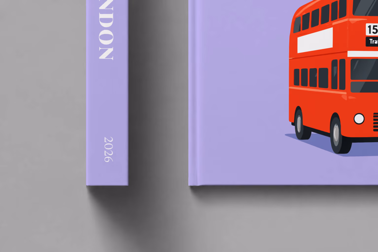 London hardcover photo book with the illustrated cover of a red double-decker London bus to Oxford Circus and Trafalgar Square on lavender, shown close up beside its spine on a pale grey studio surface