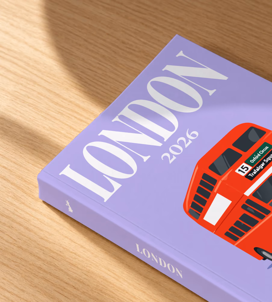London softcover photo book with the illustrated cover of a red double-decker London bus to Oxford Circus and Trafalgar Square on lavender, lying on an oak desk in dappled afternoon sunlight