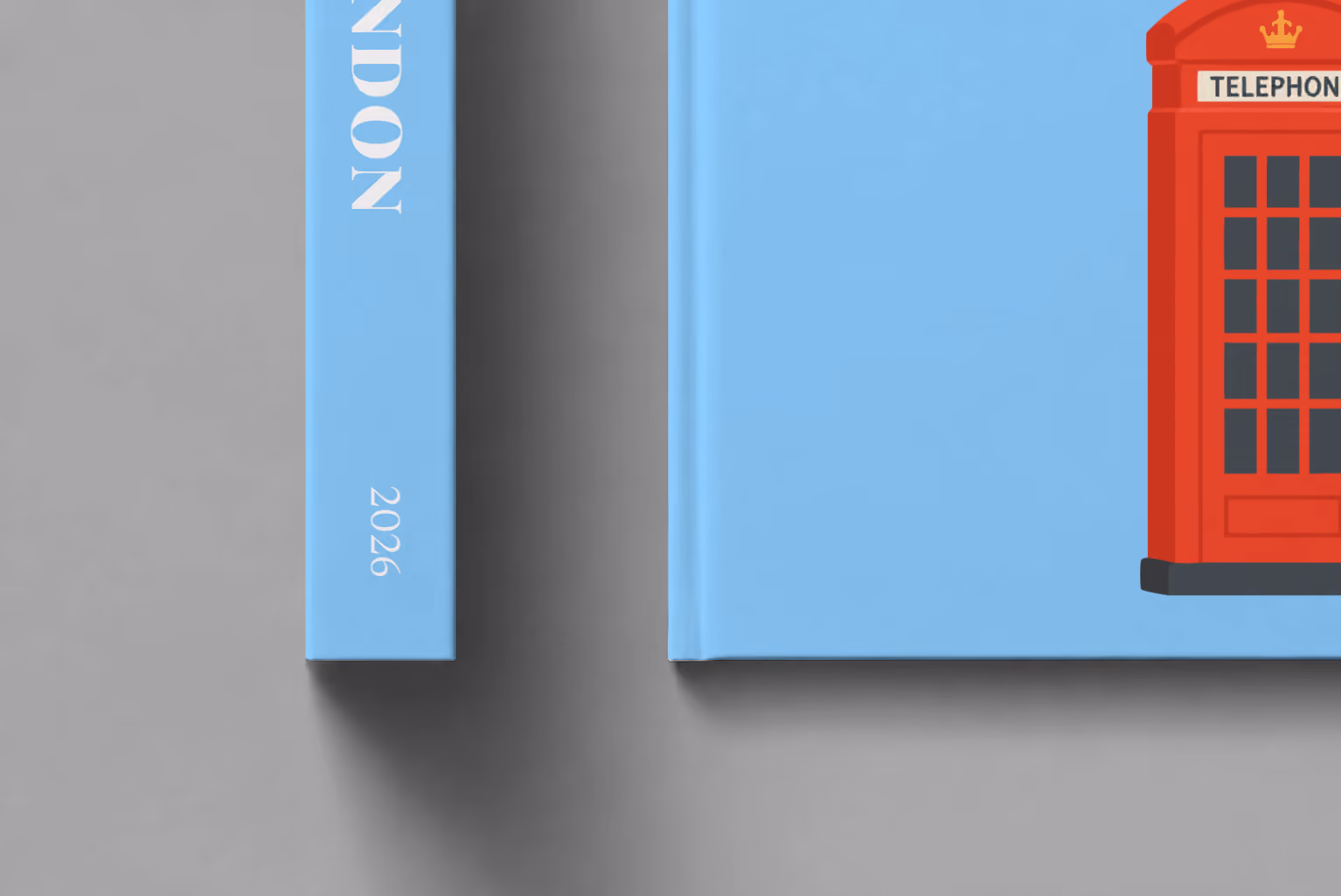 London hardcover photo book with the illustrated cover of a red London telephone box on sky blue, shown close up beside its spine on a pale grey studio surface